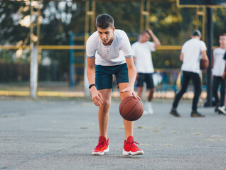 Cute boy in white t shirt plays basketball on a city playground. Active teen enjoying outdoor game...