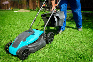 Male worker on the street working on mowing the lawn with the help of a modern lawn mower near a...