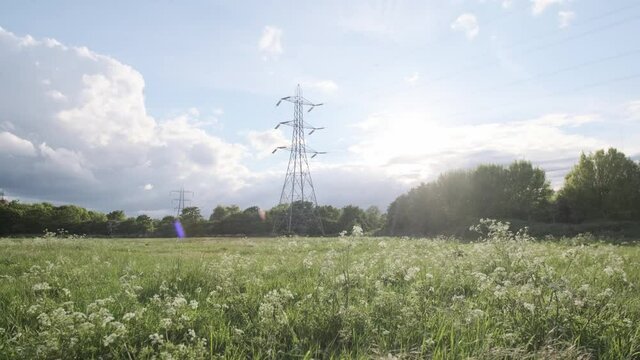 rising shot of power lines electric pylon on a sunny day green field