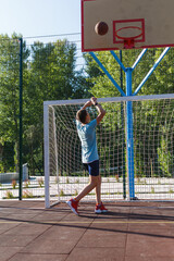Fototapeta na wymiar Cute boy in green t shirt plays basketball on a city playground. Active teen enjoying outdoor game with orange ball. Hobby, active lifestyle, sport for kids. 