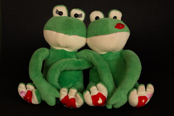 Couple of frogs touching each other on black background.