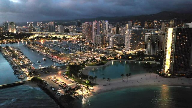 Cinematic 4K sunset, night lights aerial drone footage of marina, lagoon and hotels on the shore of Waikiki, popular tourist spot near Honolulu, Oahu island in Hawaii known for its surfing and beaches