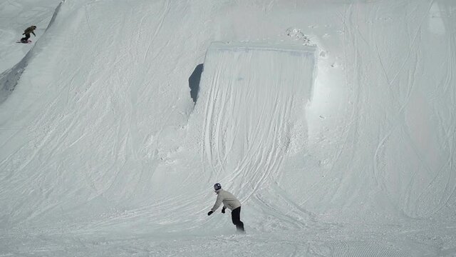 Snowboard professional rider jumping on kicker making flip and spin in snowpark on Hintertux glacier.
