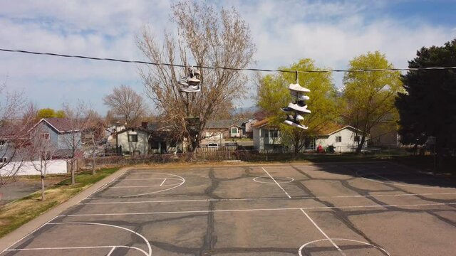 Slow pan down from shoes trainers on wrapped around telephone phone wire down to small and empty distressed basketball court after covid-19 lockdowns end. In 4k real time.