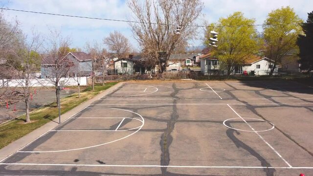 Slow pan drone clip sideways to the right of tennis shoes trainers on phone wire and a small and empty distressed basketball court after covid-19 lockdowns end. In 4k real time.