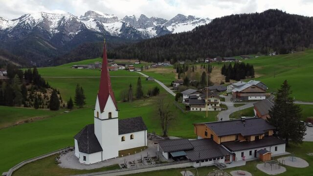 Catholic parish church of St. Lambert in Steinberg am Rofan, Austria, Tyrol. Aerial view of church and mountains in the background during a sunset.