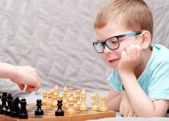 A little boy with glasses plays chess with a smile. Boy's favorite hobby. Child plays chess on the...