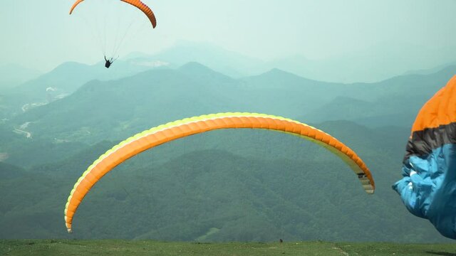Tandem paragliding in Danyang, South Korea. Paraglider jumping from the hill with instructor catching the wind, mountains landscape on background, close-up back view static,
