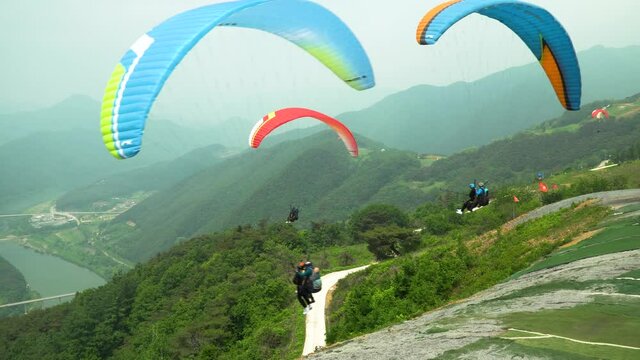 Group of people simultaneously tandem paragliding from the Mountain in Danyang, South Korea. Group of paragliders takes off from a hill one by one