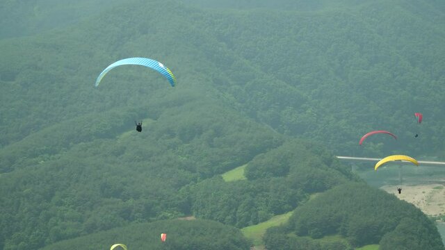 Many Tandem paragliders slowly gliding down on green mountains background in Danyang city, South Korea