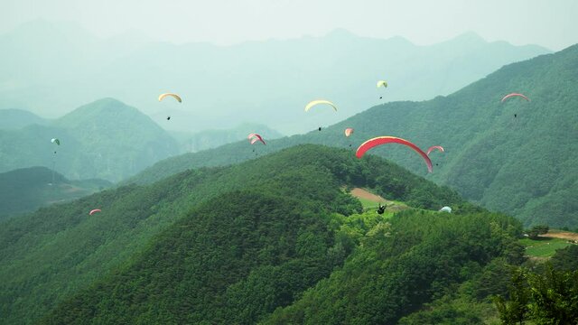 Paraglider taking off from the top of the hill and gliding towards many other people flying around green mountains in Danyang city, South Korea