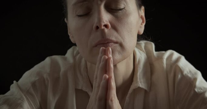 Woman implore the God. A woman pray for her children on the black background. A concept of speaking with God in silence.
