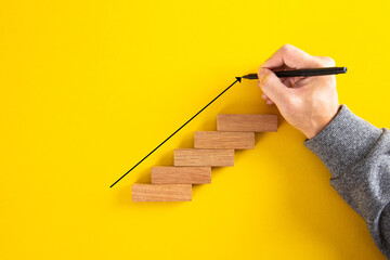 Man hand drawing an upward pointing arrow on top of growing graph made of wooden block.