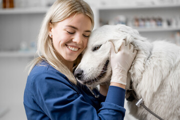 Happy female veterinarian hugs the patient big white dog standing at examination table after...