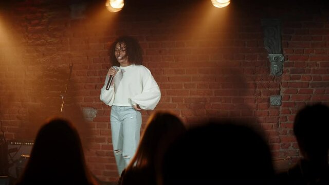 HANDHELD Black African American young female comedian performing her stand-up monologue on a stage of a small venue. Shot with ARRI Alexa Mini LF with 2x anamorphic lens