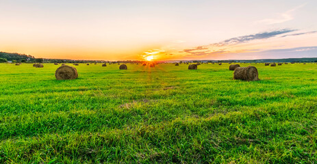 Scenic view at beautiful sunset in a green shiny field with hay stacks, cloudy sky, golden sun rays, anazing summer valley evening landscape