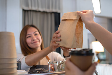 A waitress holding and serving coffee and a takeaway food in paper bag to customer in a shop