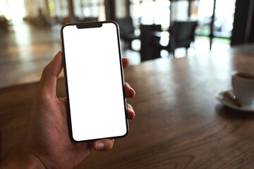 Mockup image of a man holding black mobile phone with blank white screen in cafe