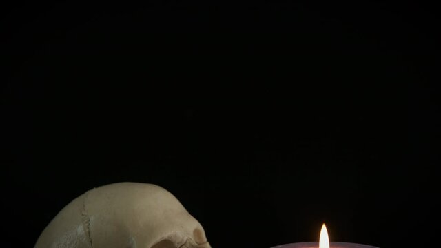Religion in a skull. A ritual with a human skull by a burning candle in the black background.