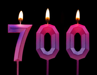 Burning birthday candles isolated on black background, number 700