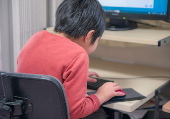 パソコンで作業する小学生の子供。猫背。在宅学習