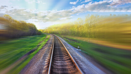 Railway track with motion blur effect. Blurred railway. Industrial conceptual landscape with blurred railway tracks and nature around. Blue sky with colorful clouds.