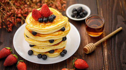 Sweet food. Stack of delicious pancakes with blueberries, Strawberry and honey in white plate on blur wooden background.