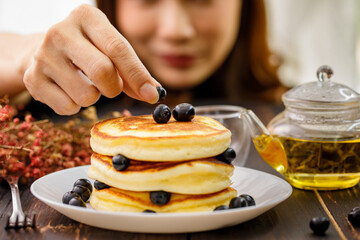 Close up hand. A woman holding hand decorating Pancake by picking up blueberries and blur teapot background. Concept sweet food.
