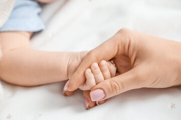 Hand of mother and cute little baby on bed, closeup