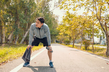 a tired young man resting and breathing holding a bottle of drinking water and towel on the road in...
