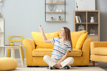 Beautiful young woman with air conditioner remote control in living room