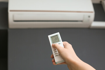 Female hand with air conditioner remote control indoors, closeup