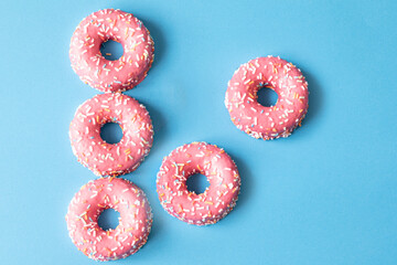 pink frosted donut with colorful sprinkles on blue background. copy space