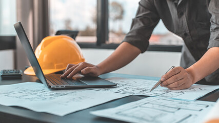 Young man with a laptop plotting a system of building structures in blueprints, Architects or...