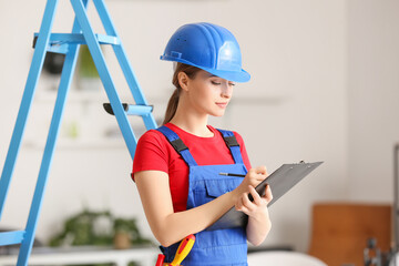 Beautiful female electrician writing in clipboard in room