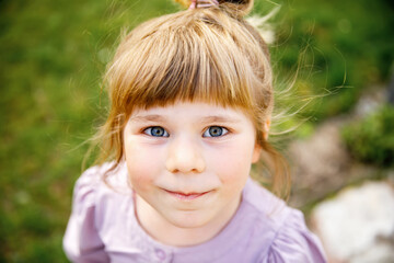 Portrait of happy smiling toddler girl outdoors. Little child with blond hairs looking and smiling at the camera. Happy healthy child enjoy outdoor activity and playing.