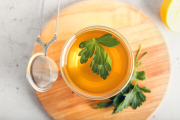 Board with cup of hot tea, parsley and lemon on light background