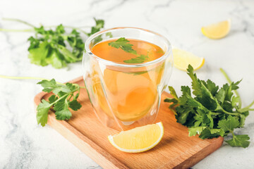 Board with cup of hot tea, parsley and lemon on light background, closeup