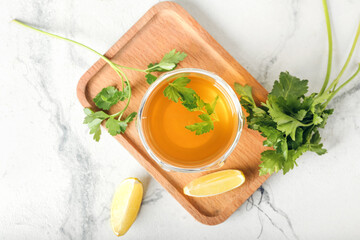 Board with cup of hot tea, parsley and lemon on light background