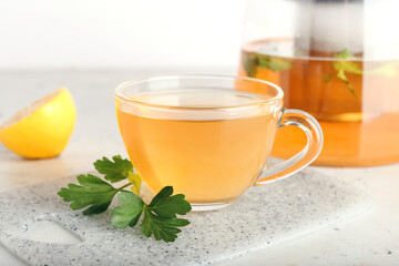 Teapot and cup of hot tea, parsley and lemon on light background