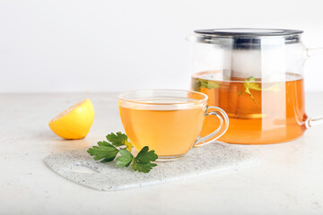 Teapot and cup of hot tea, parsley and lemon on light background