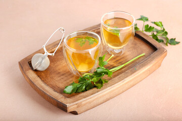 Board with cups of hot tea and parsley on color background