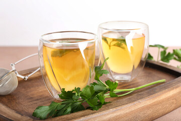 Board with cups of hot tea and parsley on light background