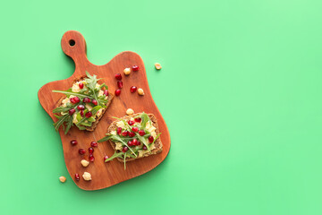 Tasty bruschettas with pomegranate and hummus on color background