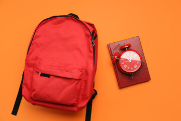 School backpack, notebook and alarm clock on color background