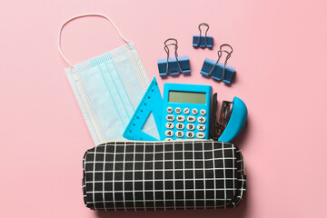 Pencil case with stationery and medical mask on color background