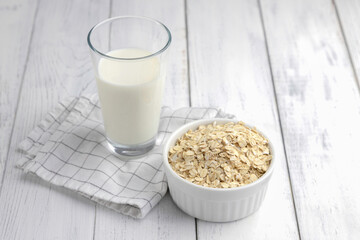 Oatmeal, vegetable milk in a glass and oat flakes near on a white wooden background. Close-up. Alternative milk for vegetarians and vegans.