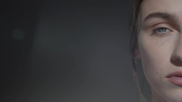 Close Up Half Of Face Shot Of Beautiful Young Woman With No Makeup Posing For Camera Against Dark Background With Copy Space On Left Side