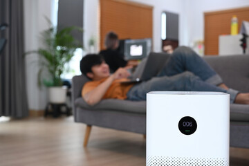 Air purifier in living room and young man resting on sofa.