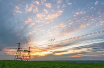 Obraz premium High voltage lines and power pylons in a flat and green agricultural landscape on a sunny day with cirrus clouds in the blue sky